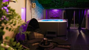 An outdoor hot tub area with a stone wall, wicker furniture, and a glass door leading to a patio.