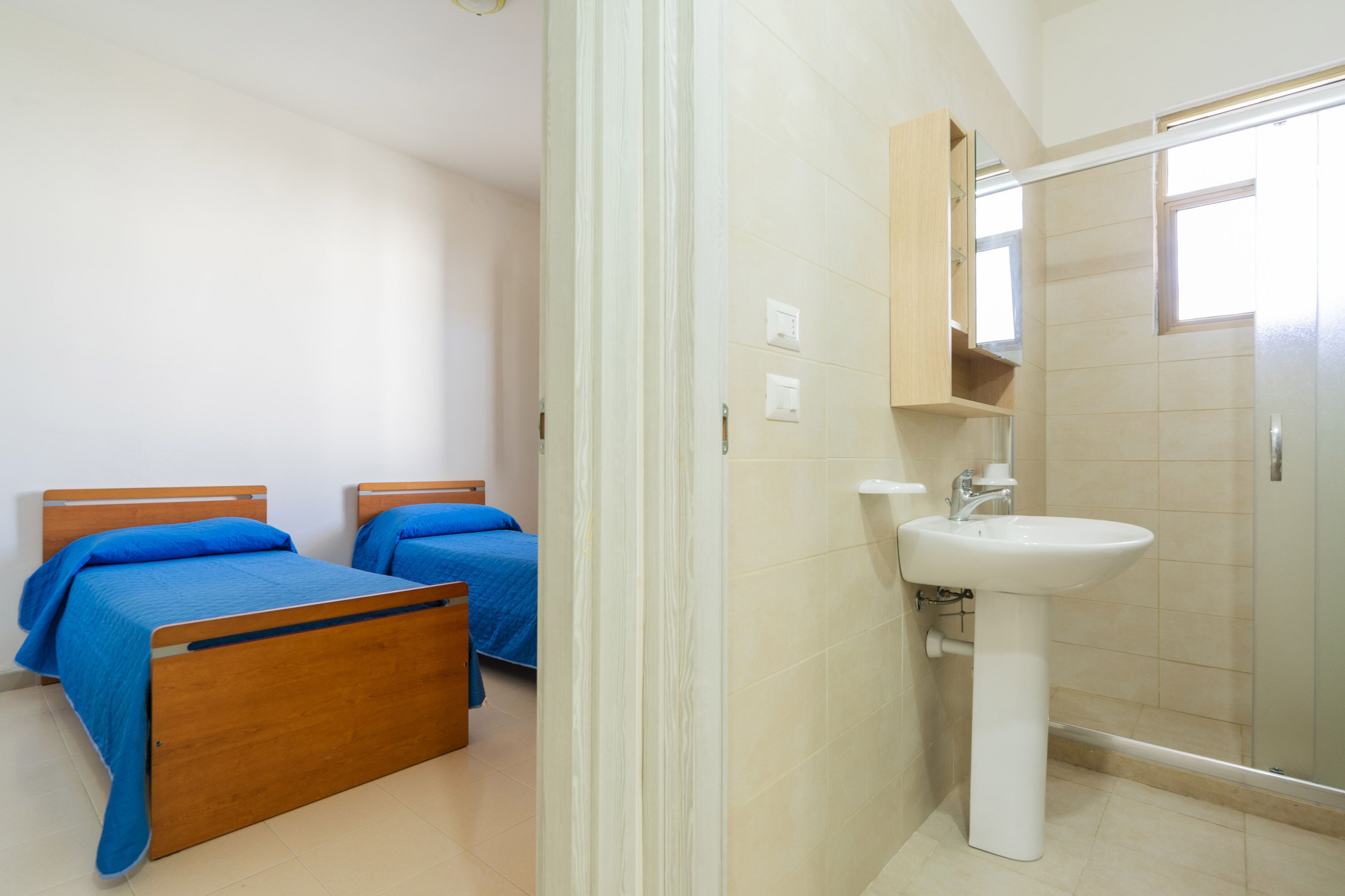 A bedroom with two wooden beds, a bathroom with a sink and mirror, and a shower.