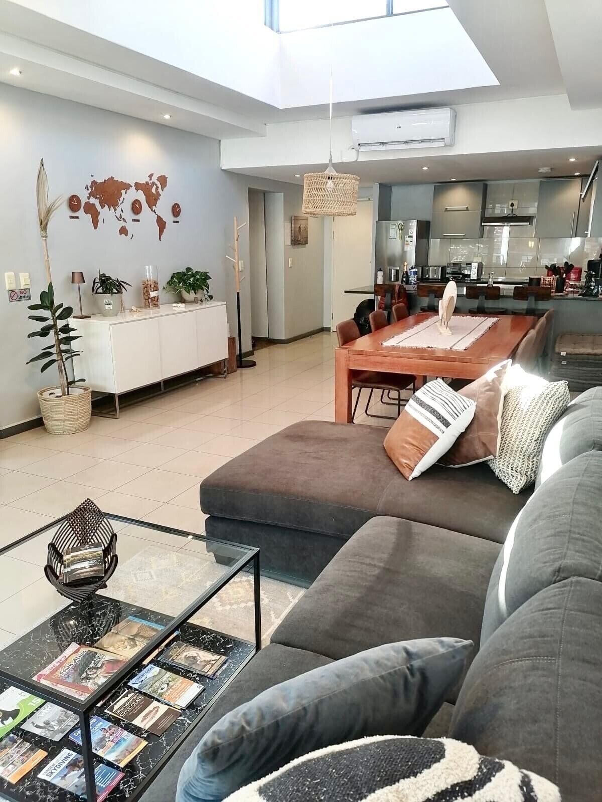 Un salon moderne avec un canapé, une table basse sur laquelle sont posés des livres, un coin repas avec une table en bois, et une cuisine en arrière-plan.