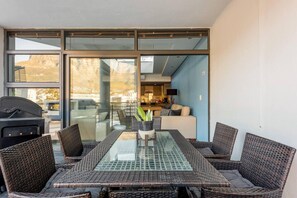 A sunlit patio with a glass-top table and wicker chairs, overlooking a cityscape. - 3-bed, Sleeps 6, Free Parking (Cape Town)