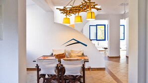 Un comedor con una mesa y sillas blancas, una lámpara decorativa en el techo y vistas de la habitación contigua.
