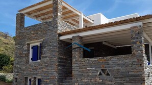 Un edificio de piedra con estructura de techo de madera, una ventana con contraventanas azules y un nivel superior en construcción.