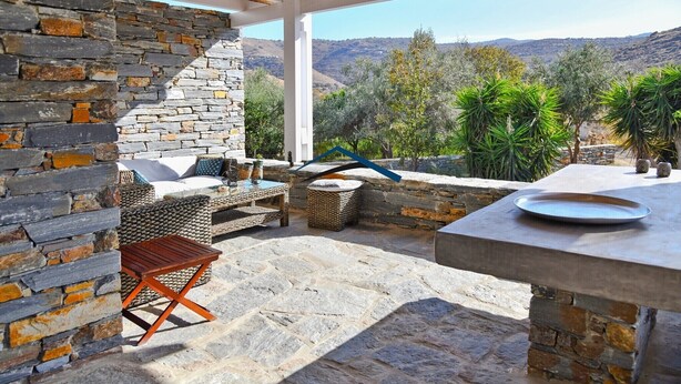 Un patio al aire libre con paredes de piedra, una mesa de madera y vistas a un paisaje montañoso.