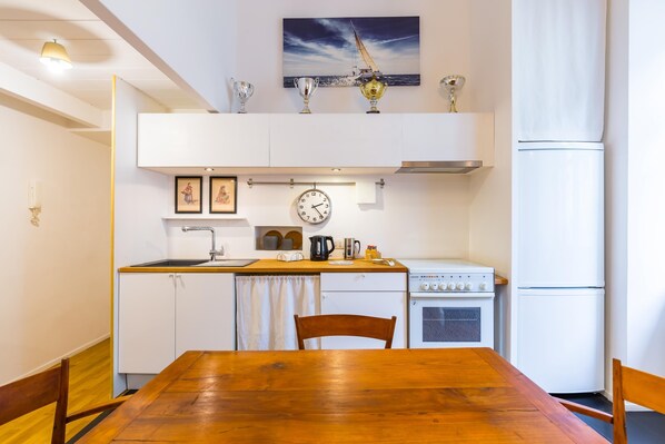 A compact kitchen with a wooden dining table, white cabinetry, a stove, and a refrigerator.