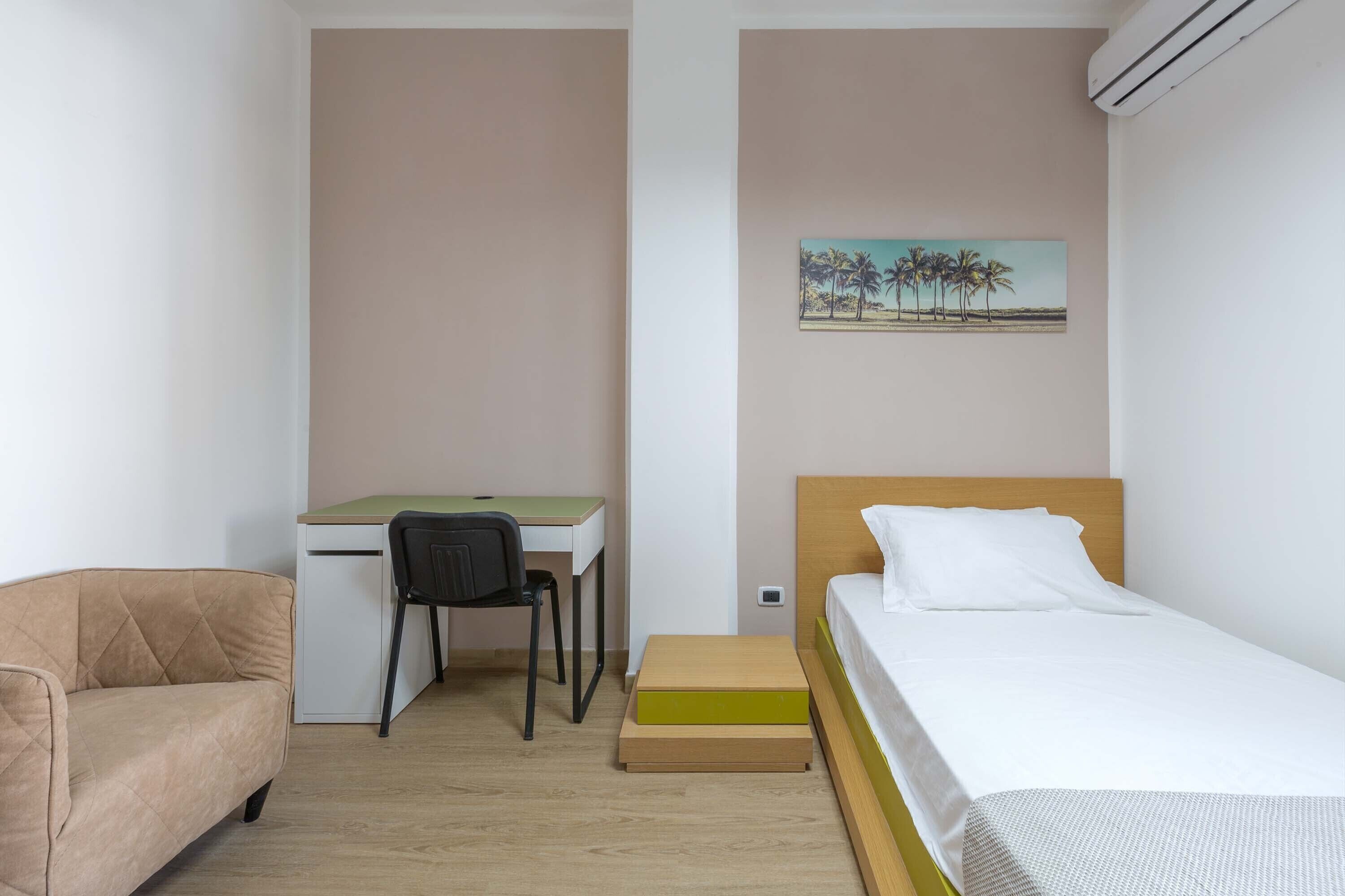 Een kleine, verzorgde kamer met een bed, een bureau en een stoel.