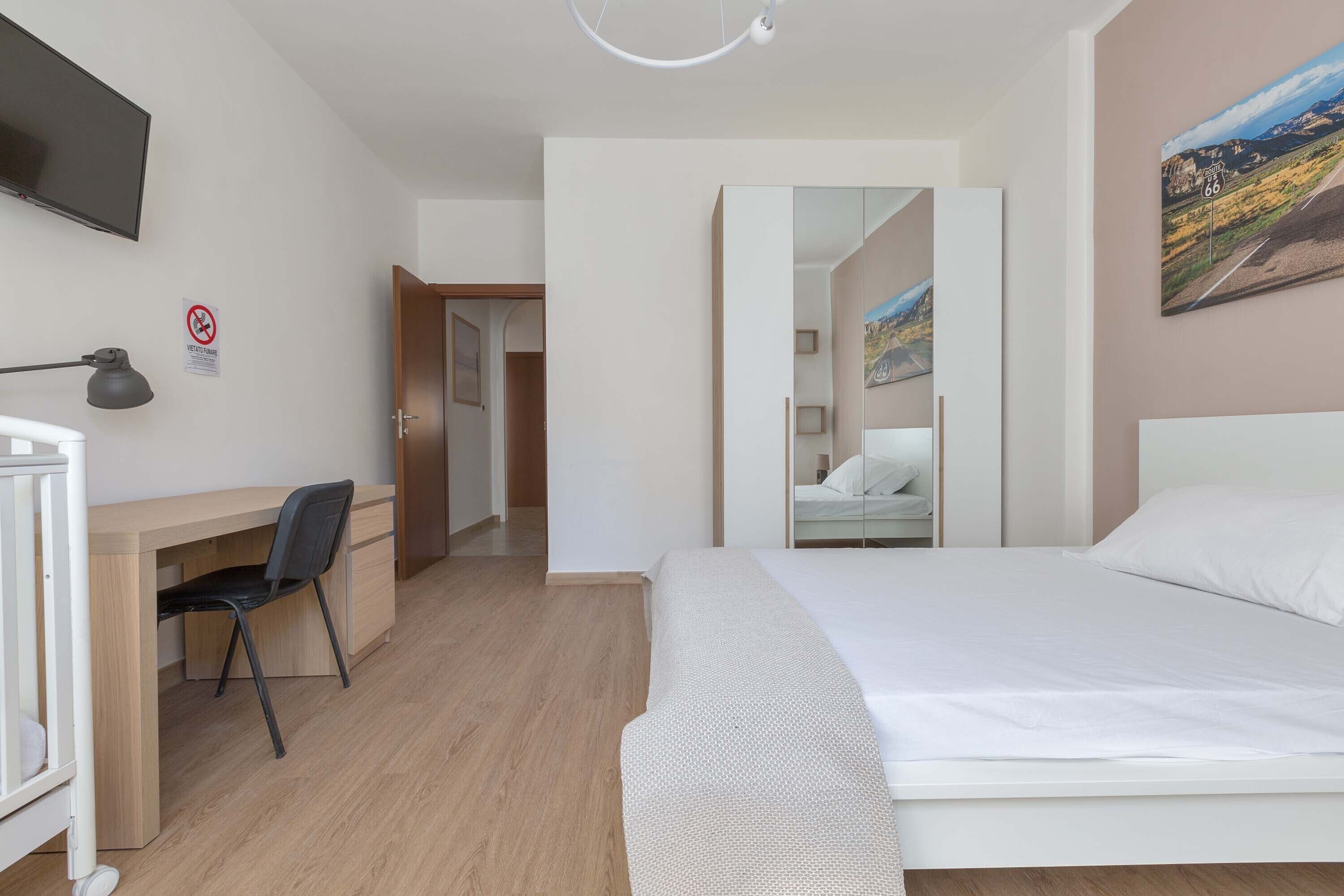 Ein Hotelzimmer mit Bett, Schreibtisch, Stuhl und einem an der Wand befestigten Fernseher.