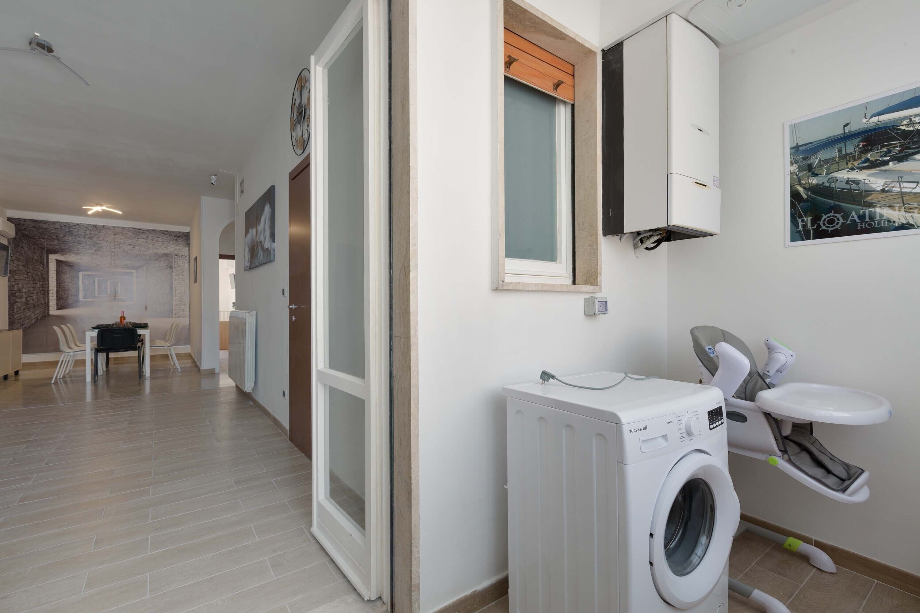 A modern hotel room with a washing machine, a built-in toilet, and a dining area in the background.