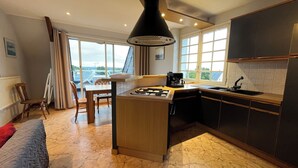 Een moderne keuken met een centraal eiland, een gasfornuis en een koffiezetapparaat. Er is een eethoek met een tafel en stoelen, en grote ramen met uitzicht.