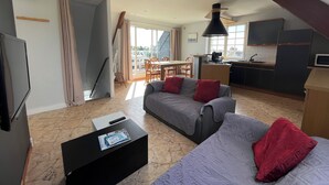 Een moderne woonkamer met een bank, een salontafel en een televisie. Er is een eethoek met een tafel en stoelen, en een keuken met een fornuis en kastjes.