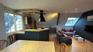 Een moderne keuken met een centraal eiland, een eethoek met tafel, en een zithoek met bank en televisie.
