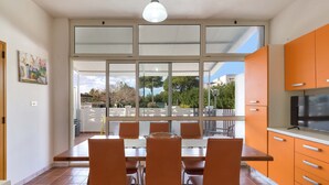 A modern kitchen with orange cabinets, a dining table with chairs, and a large window overlooking a garden. - 2727 Villetta Chiara Blu Piano Terra by Barbarhouse (Melendugno)