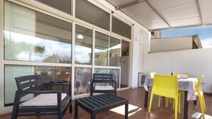 An outdoor patio area with a table and chairs, a bench, and a sliding glass door leading to a balcony. - 2727 Villetta Chiara Blu Piano Terra by Barbarhouse (Melendugno)