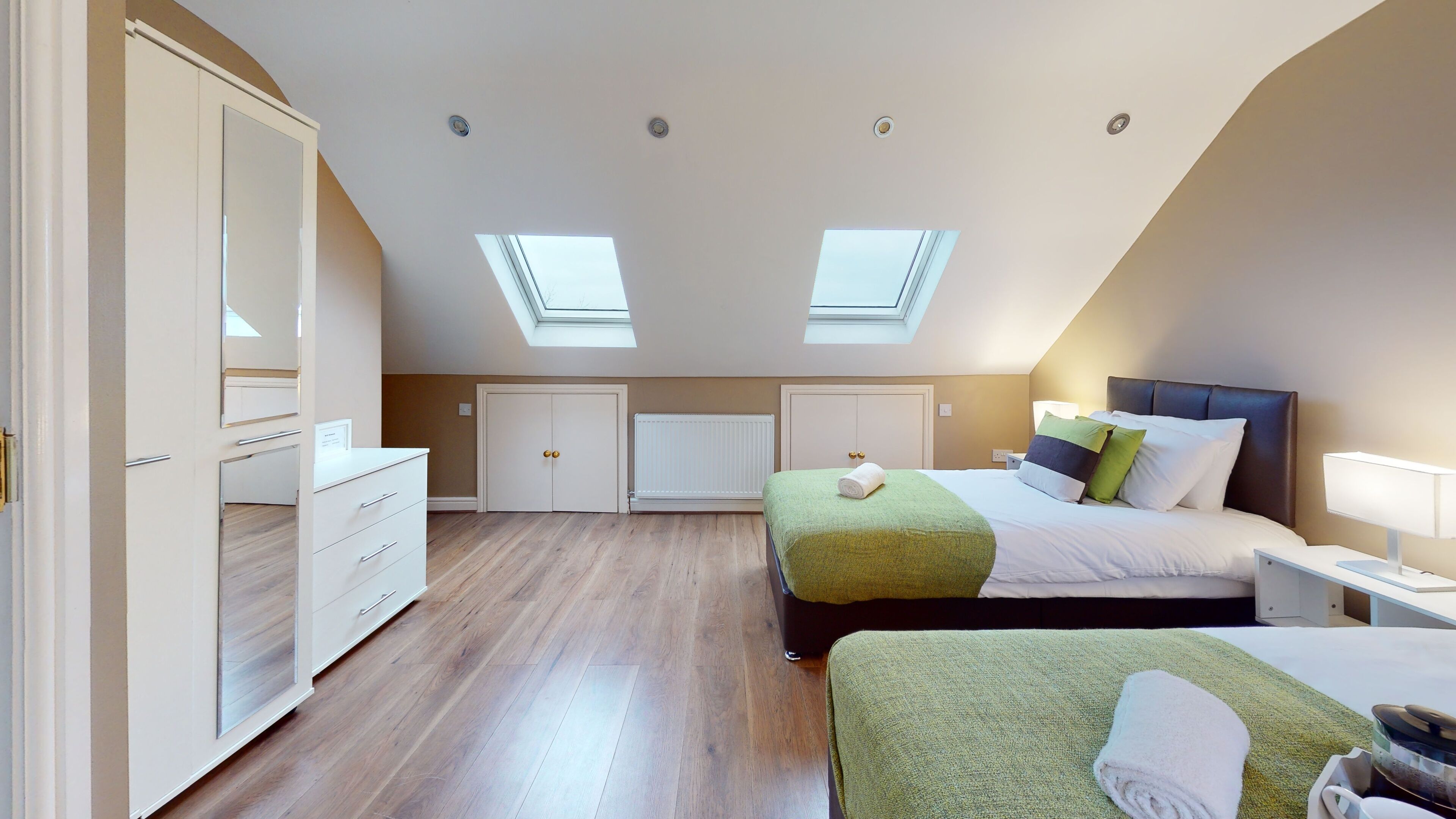 A bedroom with a sloped ceiling, skylights, a bed with pillows, a bedside table with a lamp, and a dresser.