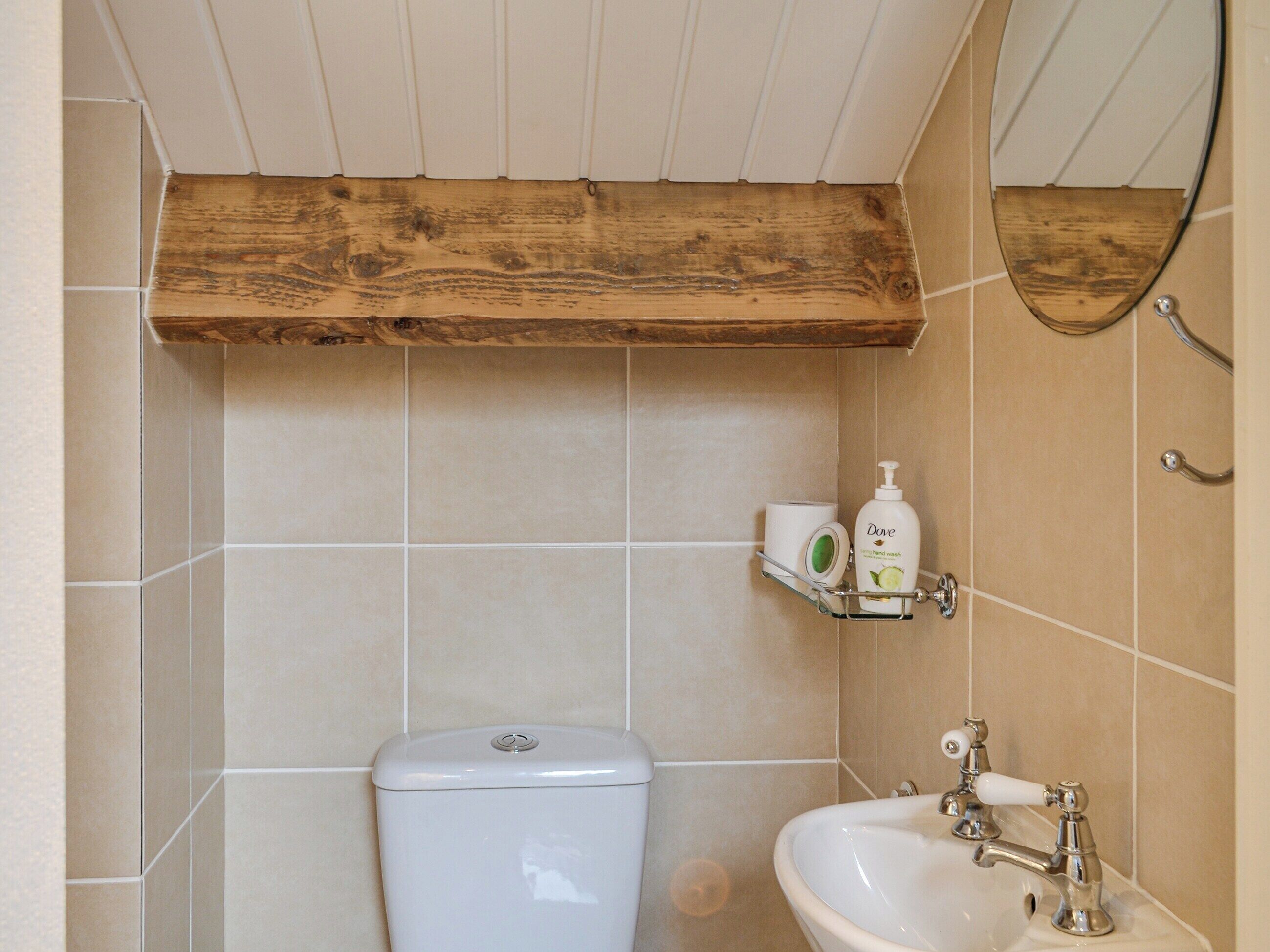 A bathroom with a toilet, sink, and wooden shelf with toiletries.