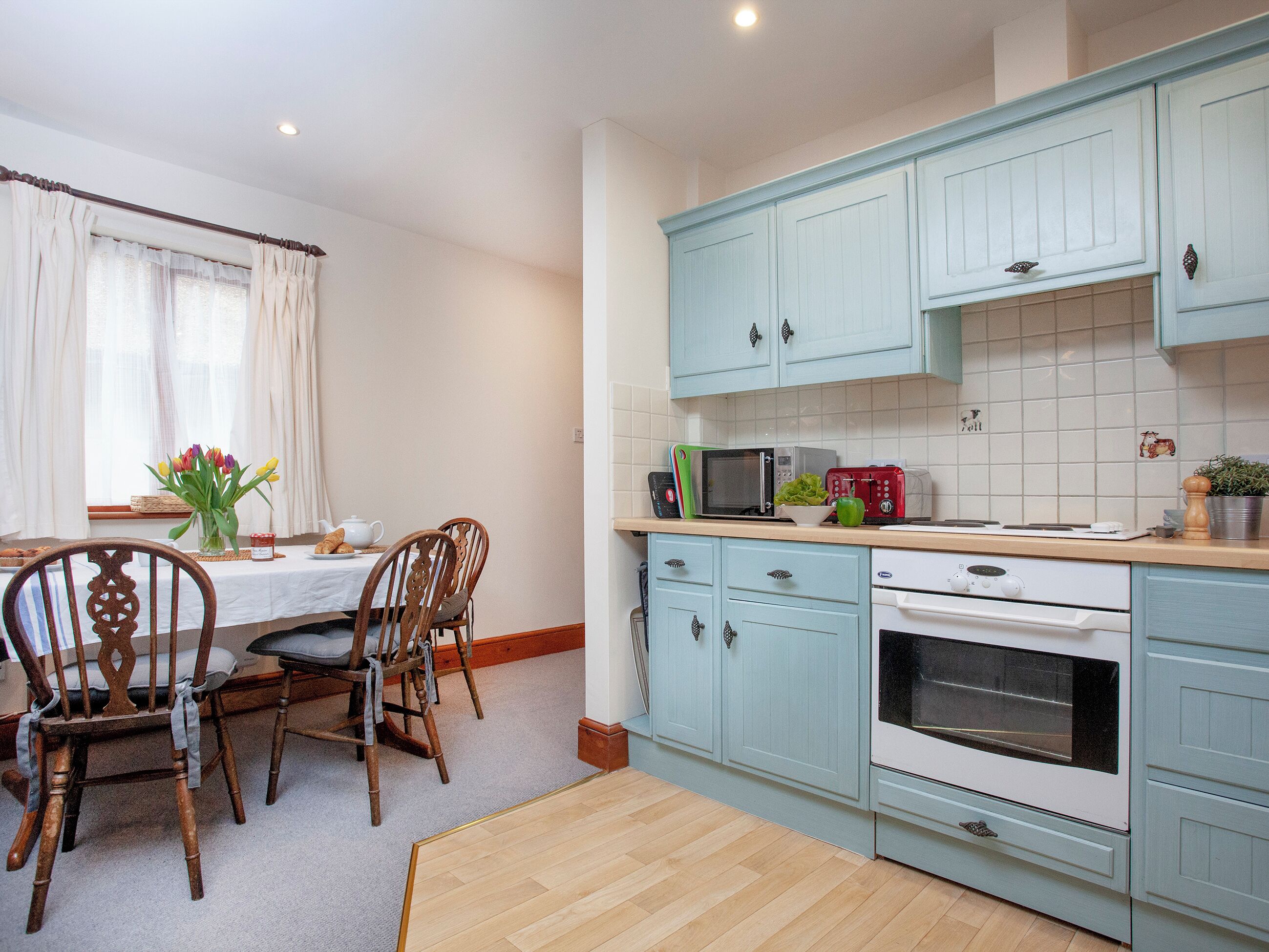 Une cuisine avec des meubles de couleur bleu clair, une table à manger en bois avec des chaises, un four à micro-ondes, un grille-pain et une cuisinière.
