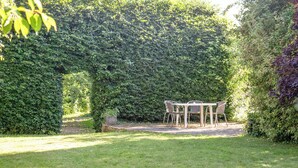 A garden with a table and chairs under a dense hedge. - 2 bedroom accommodation in Clyst Honiton, near Exeter (Clyst Honiton, near Exeter)