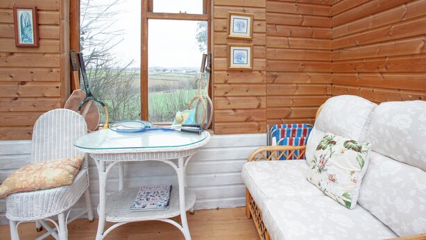 A cozy room with wooden walls, a wicker chair, a white sofa, a glass table, and a view of the countryside. - 2 bedroom accommodation in Clyst Honiton, near Exeter (Clyst Honiton, near Exeter)