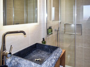 A bathroom with a marble sink, a handheld showerhead, and a glass-enclosed shower area.