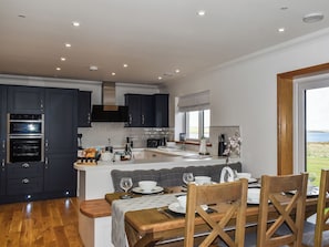 Una cocina moderna con armarios oscuros, un comedor con sillas de madera y vistas al exterior a través de un ventanal.