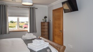 A hotel room with a bed, a TV mounted on the wall, a wooden wardrobe, and a window with curtains. - Uninterrupted views over Coll Beach and sea views out over Broadbay. (All Outer Hebrides)