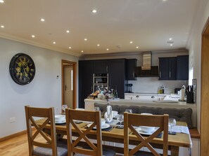 Une cuisine moderne avec des meubles de couleur sombre, un îlot central et un coin repas comprenant des chaises en bois et une table mise pour le repas.