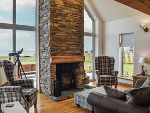Un salón acogedor con chimenea de piedra, muebles a cuadros y ventanas amplias que ofrecen vistas al exterior.