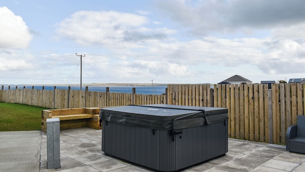 A hot tub in a backyard with a wooden fence, a bench, and a view of the sea.