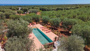 Vista aérea de un resort con una piscina rectangular rodeada de sillones de descanso y un paisaje desértico.