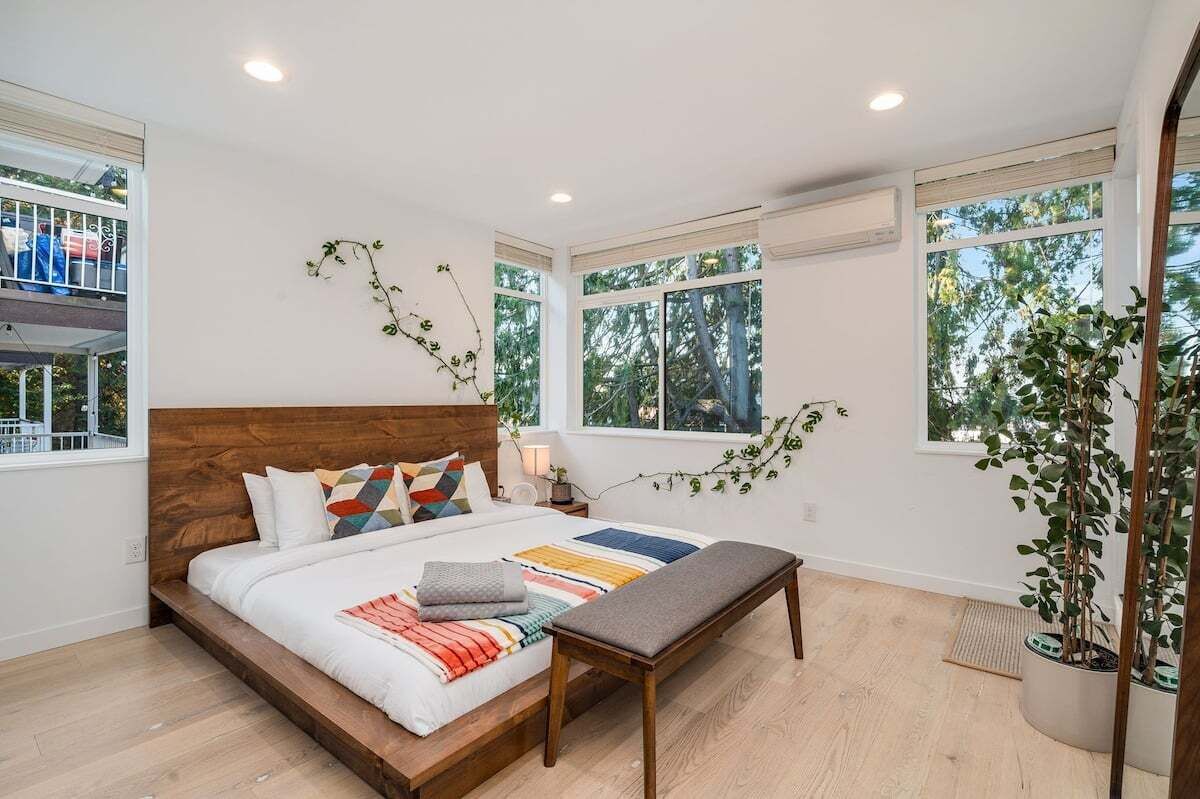 Une chambre à coucher avec un lit en bois, de nombreuses fenêtres et des plantes d’intérieur.