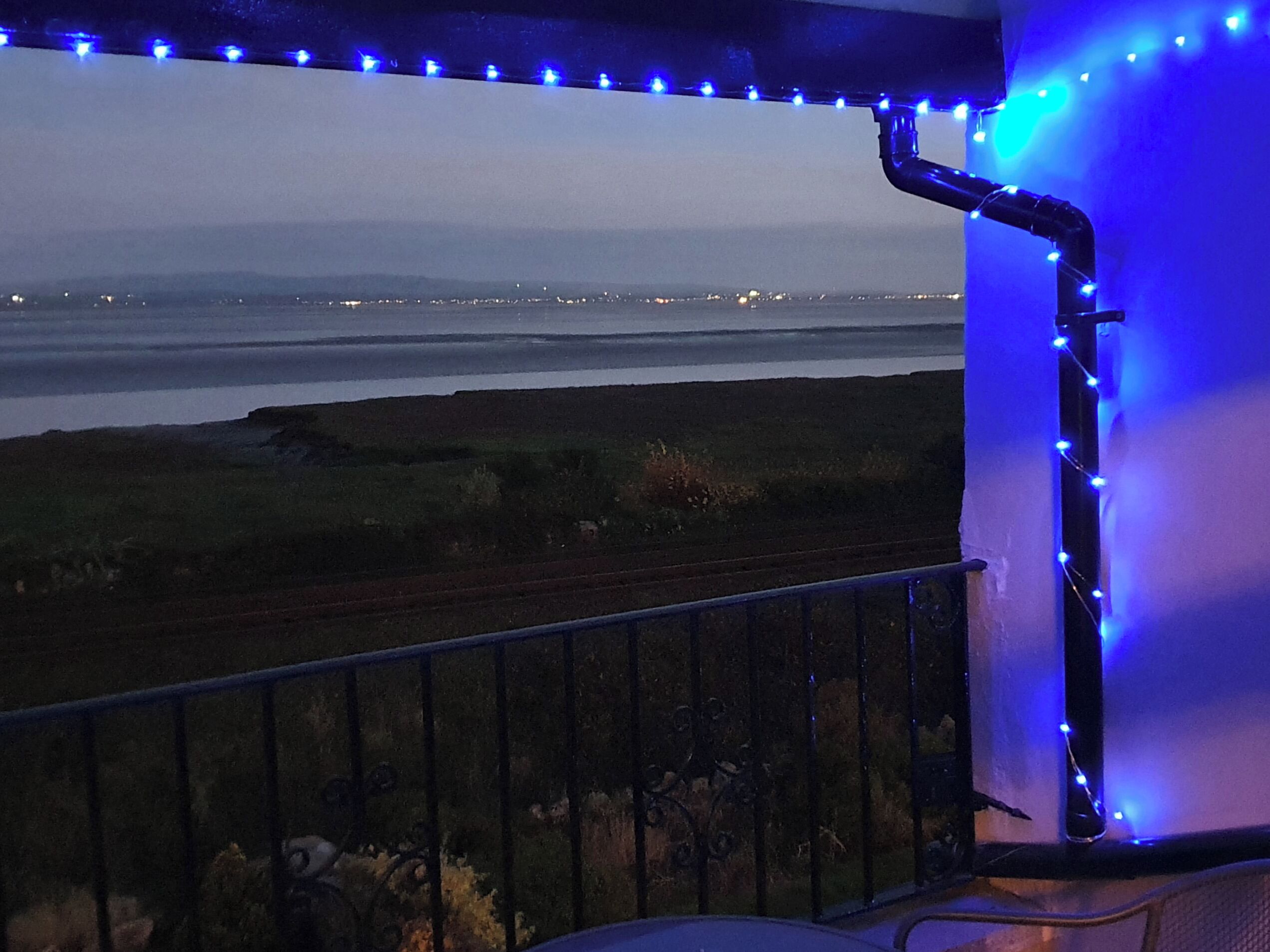 A balcony with a view of a body of water and distant city lights.