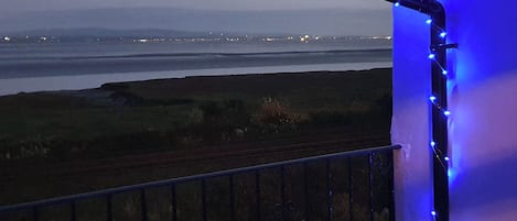 A balcony with a view of a body of water and distant city lights.