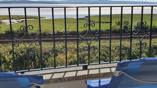 A balcony with a view of a railway track, greenery, and distant hills.