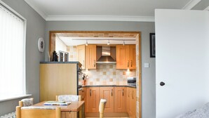 A compact kitchen with wooden cabinets, a dining table with chairs, and a black leather couch.