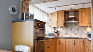 A modern kitchen with wooden cabinets, a built-in oven, and a dining area with a table and chairs.