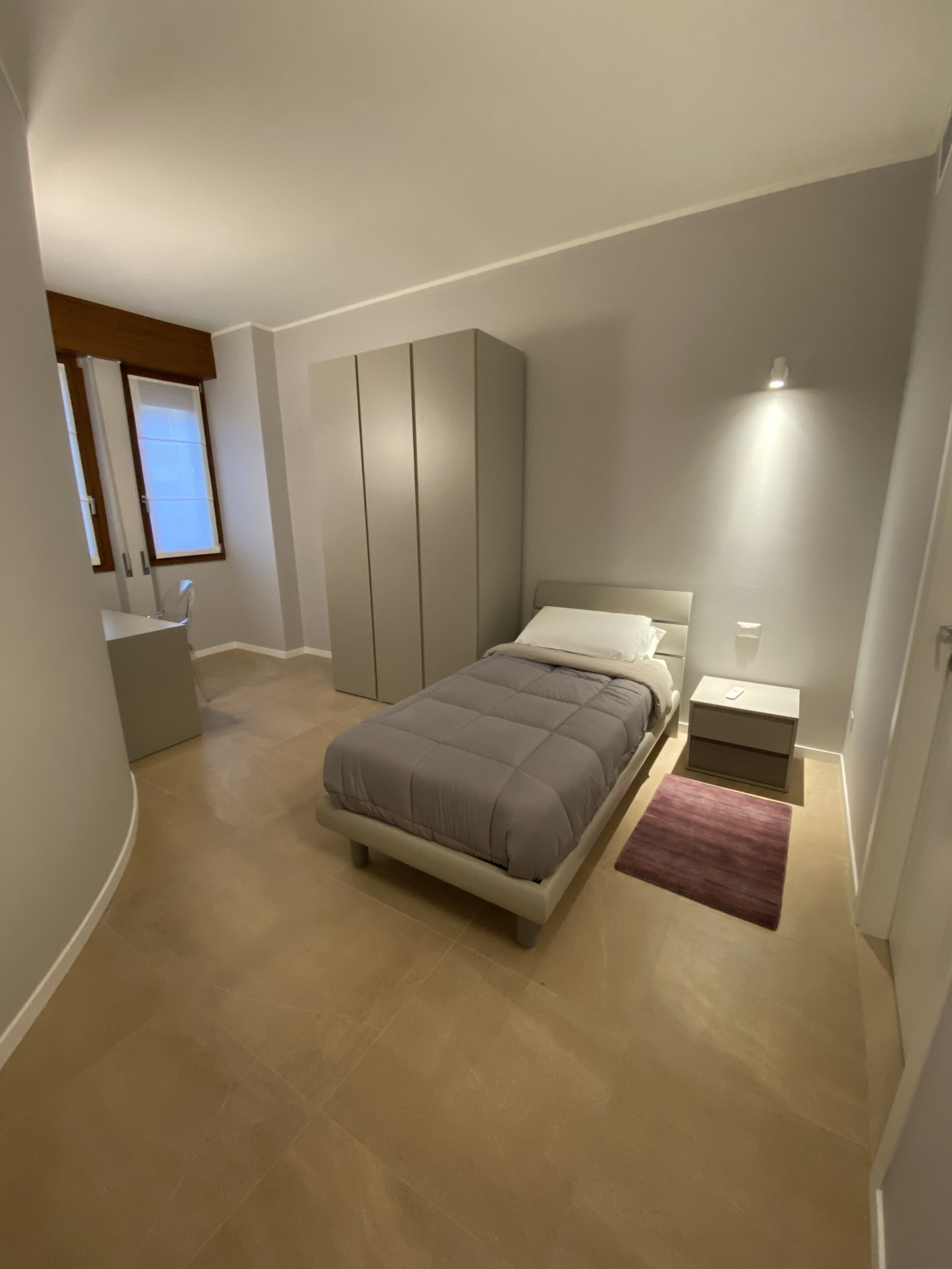 Une chambre à coucher moderne avec un lit, une table de chevet, une armoire et un petit bureau.