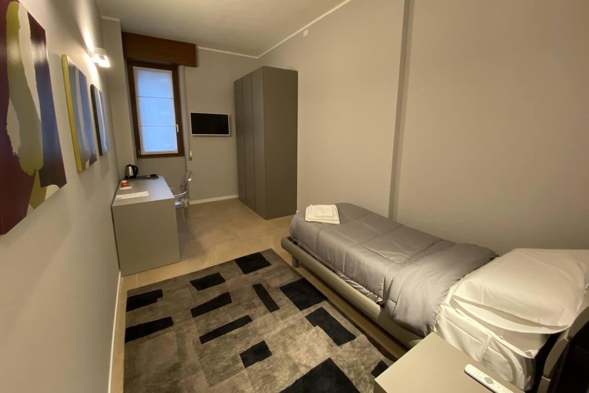 Une chambre d’hôtel de taille réduite, comprenant un lit, un bureau, une chaise, une télévision et une armoire.