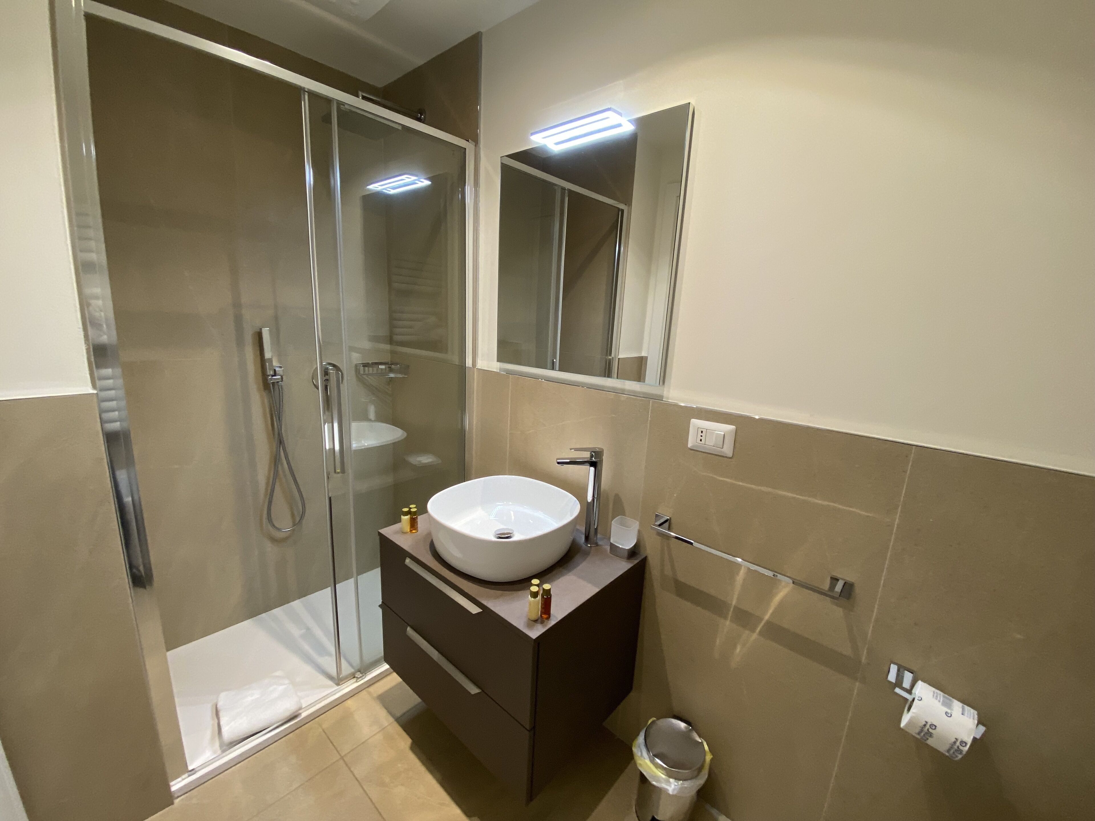 Un baño moderno con ducha envuelta en vidrio, un lavabo blanco y un espejo encima.