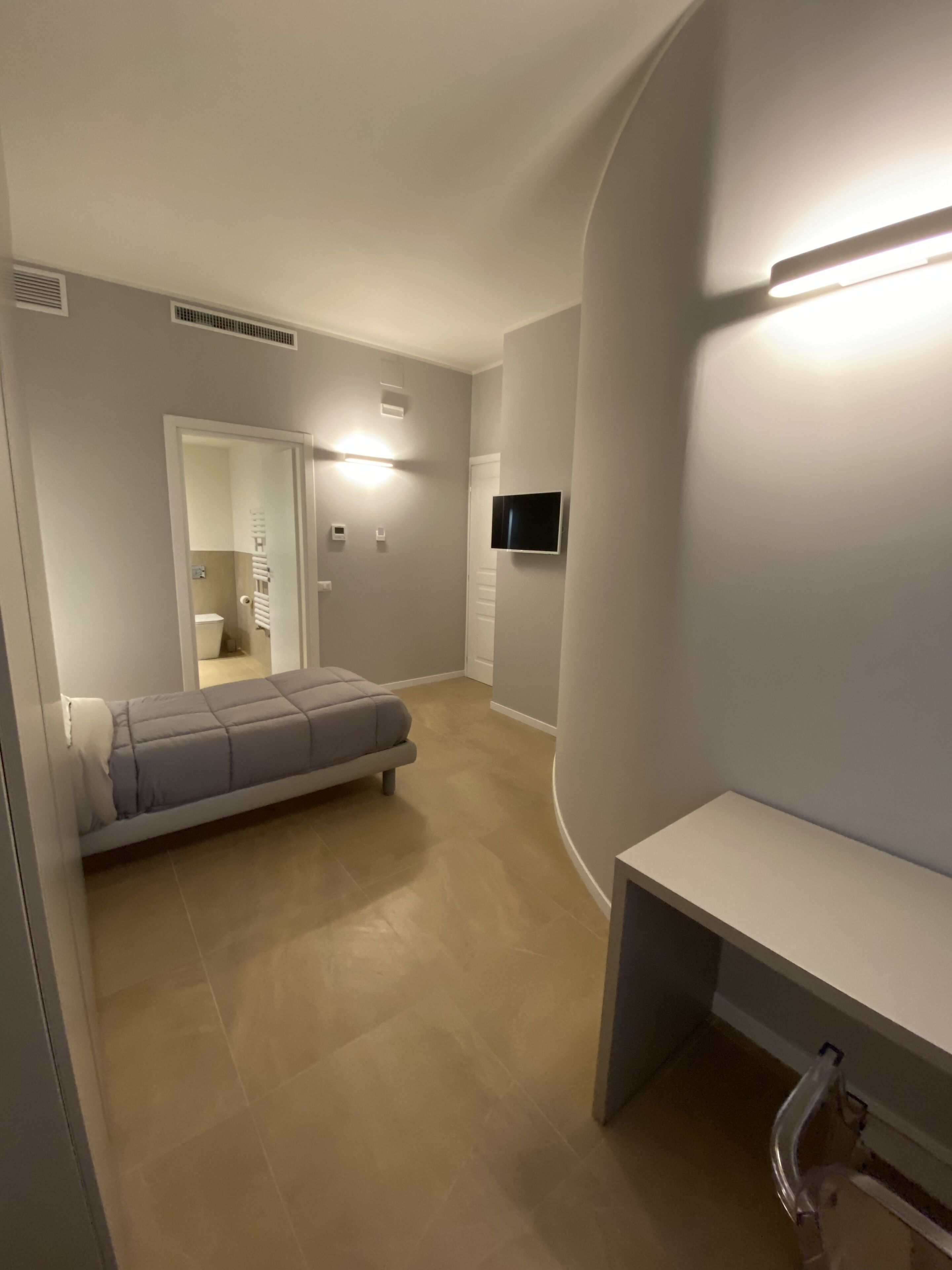 A modern bedroom with a bed, a desk, and a TV.