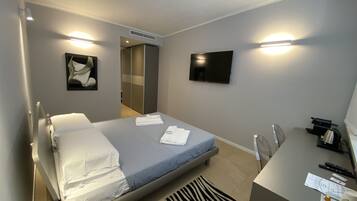 Ein Hotelzimmer mit Bett, Schreibtisch, Stuhl, Fernseher und einem Bild an der Wand.