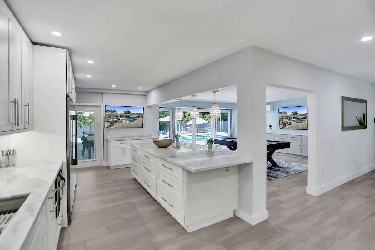 A spacious kitchen with a large island, white cabinetry, and a view of a pool through the glass door.