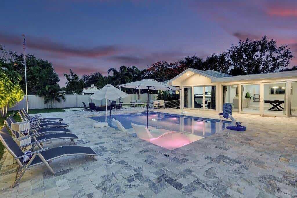 Une piscine entourée de chaises longues et de parasols, le tout bordé d’un bâtiment doté de portes vitrées.