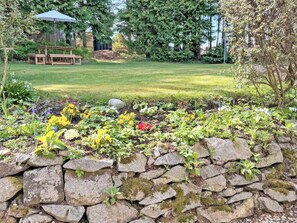 A stone wall with plants, a grassy lawn, and a picnic table in a garden setting.