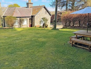 A stone house with a grassy yard, a wooden bench, and a picnic table. - 2 bedroom accommodation in Alford (Alford)
