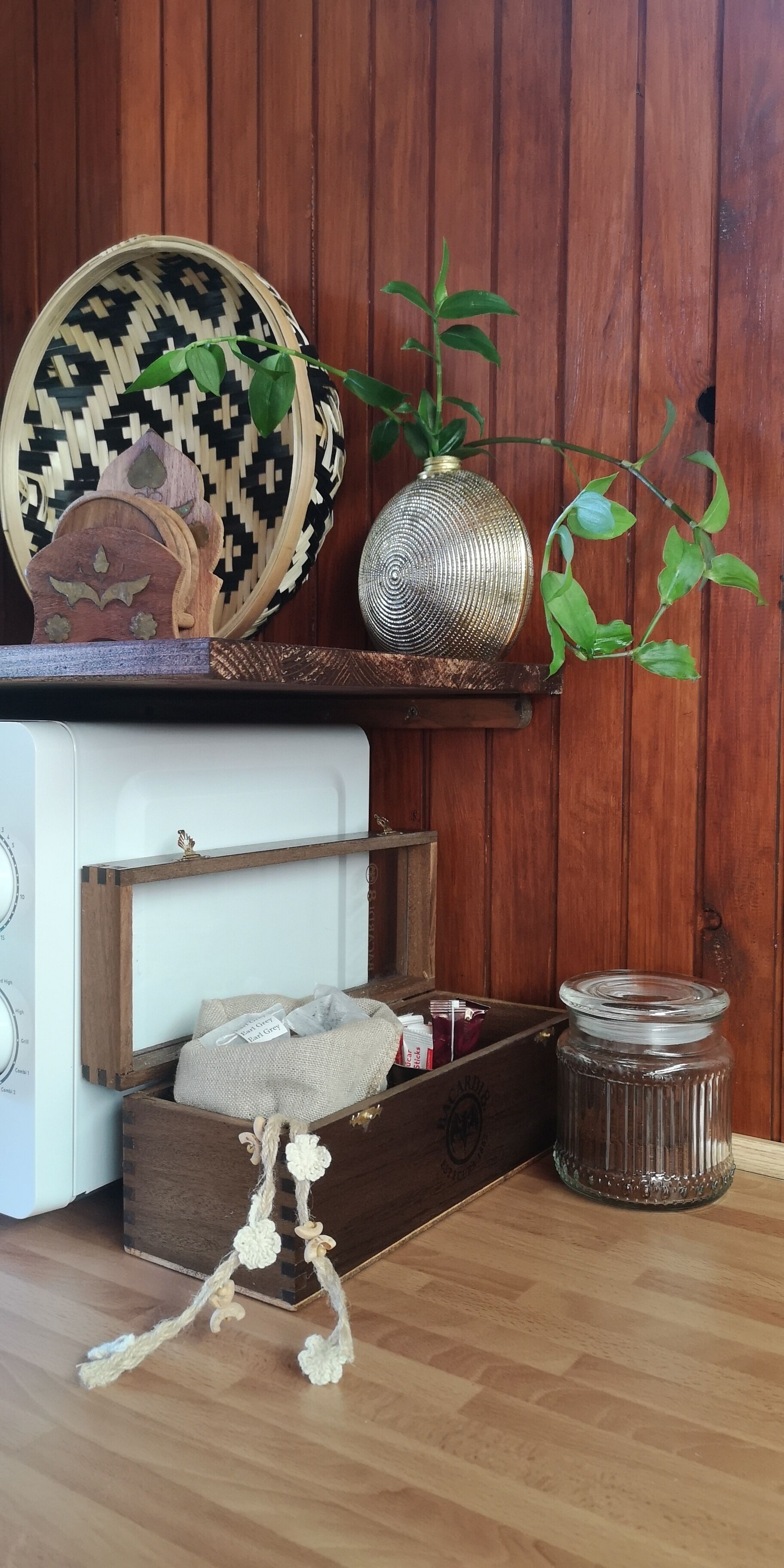 A wooden cabinet with a woven basket, a glass vase, and a wooden box with a label.