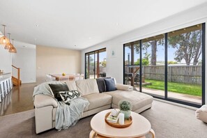 Un salon moderne avec un grand canapé d’angle, une table basse ronde et une vue sur le jardin à travers de grandes fenêtres.