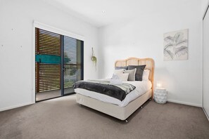 Une chambre à coucher comprenant un lit, une table de chevet, une plante fixée au mur et une porte coulissante avec des stores.