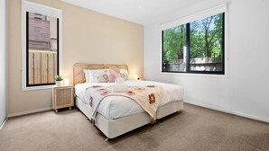 Een slaapkamer met een bed, nachtkastje, raam en uitzicht op bomen.