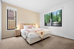 Une chambre à coucher avec un lit, une table de chevet, une fenêtre et une vue sur les arbres.