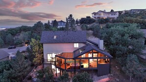 A modern house with a large glass extension, surrounded by trees and a view of other houses. - Broadmoor Luxury Retreat - Mountain View & Hot Tub (Colorado Springs)