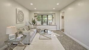 A living room with a sofa, coffee table, and lamp. There is a window with plants and a painting on the wall. - Broadmoor Luxury Retreat - Mountain View & Hot Tub (Colorado Springs)
